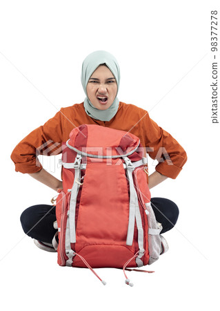 Asian Muslim woman in a headscarf sitting with a backpack with an upset expression Asian Muslim woman in a headscarf sitting with a backpack with an upset expression 98377278