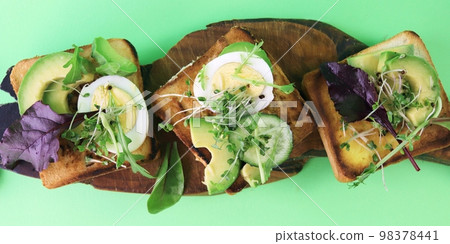 Sandwiches with avocado, boiled eggs, leek and arugula, sprinkled with fresh micro green sprouts, on a wooden board, natural ingredients, healthy food Sandwiches with avocado, boiled eggs, leek and arugula, sprinkled with fresh micro green sprouts, on a wooden board, natural ingredients, healthy food 98378441