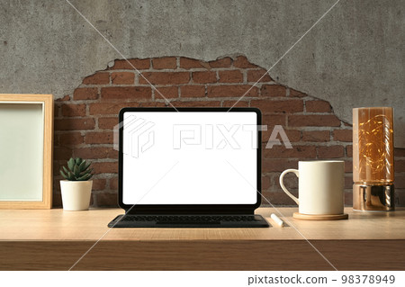 Front view of digital tablet with wireless keyboard, coffee cup, books and picture frame on wooden working desk 98378949