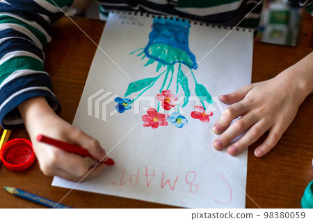 The hands of a child drawing flowers with gouache paints for mom by March 8 98380059