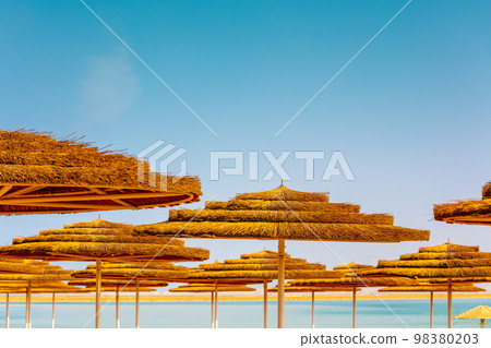 Tropical beach scenery with sun parasols. Straw sun umbrellas on the beach on a sunny day Tropical beach scenery with sun parasols. Straw sun umbrellas on the beach on a sunny day 98380203