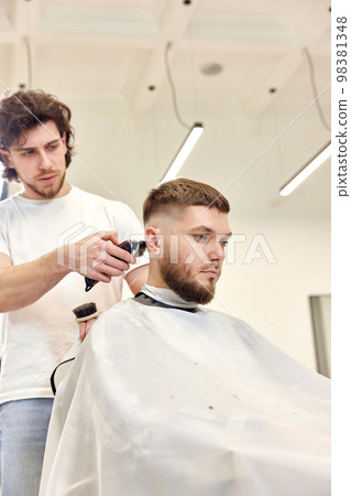 Barber trim hair with clipper on handsome bearded man Barber trim hair with clipper on handsome bearded man 98381348