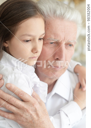 sad grandfather and granddaughter hugging at home sad grandfather and granddaughter hugging at home 98382004