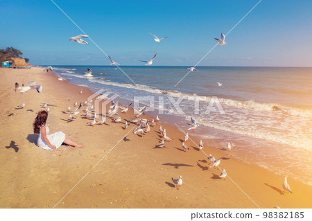 Seascape on a sunny day. Young woman sits on the beach Seascape on a sunny day. Young woman sits on the beach 98382185