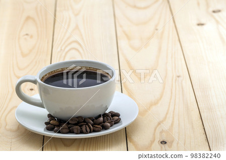 White cup with black steaming coffee on plate with coffee beans on yellow White cup with black steaming coffee on plate with coffee beans on yellow 98382240