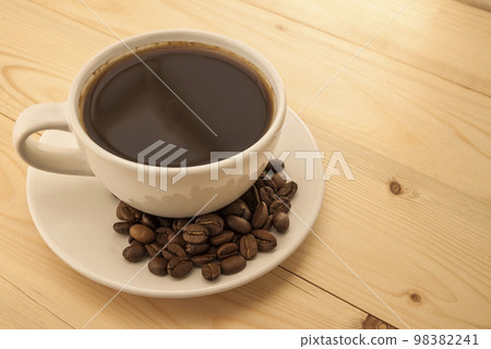 White cup with black coffee on plate with coffee beans on yellow White cup with black coffee on plate with coffee beans on yellow 98382241