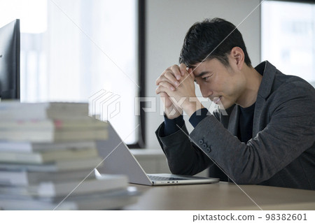 Businessman in his thirties holding his head in front of his desk laptop Businessman in his thirties holding his head in front of his desk laptop 98382601
