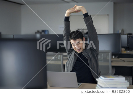 A businessman in his thirties stretching at his desk at work 98382800