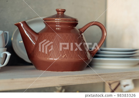 brown clay teapot on a white shelf with cups and plates brown clay teapot on a white shelf with cups and plates 98383326