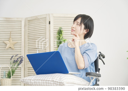 Disabled woman on a wheelchair imagining while using a computer at home 98383390