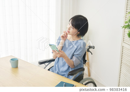 坐在輪椅上的殘疾婦女想像著家裡的智能手機 坐在輪椅上的殘疾婦女想像著家裡的智能手機 98383416