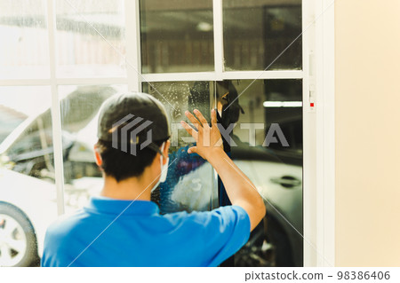 Woker wrapping tinting a house window with tinted foil. Woker wrapping tinting a house window with tinted foil. 98386406