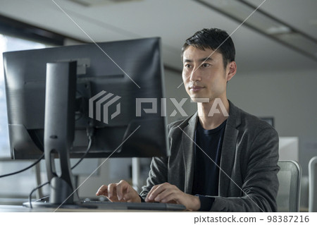 A man in his thirties working on a desktop computer 98387216