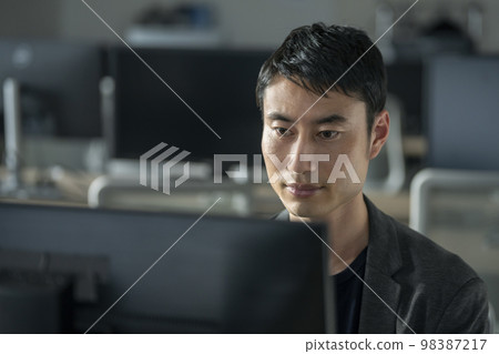 A man in his thirties staring at a PC display A man in his thirties staring at a PC display 98387217