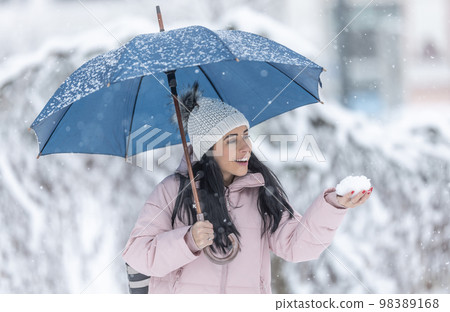 Happy woman holding an umbrella on a cold snowy day and holding fresh snow in her hand Happy woman holding an umbrella on a cold snowy day and holding fresh snow in her hand 98389168