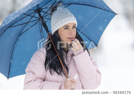Gorgeous brunette puts on lip balm dressed in warm clothes outdoors on a cold winter day Gorgeous brunette puts on lip balm dressed in warm clothes outdoors on a cold winter day 98389170