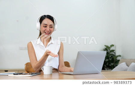 Smiling young asian woman working on laptop at home. Attractive asia female using computer remote studying, watching online education and video calling for webinar Smiling young asian woman working on laptop at home. Attractive asia female using computer remote studying, watching online education and video calling for webinar 98389373