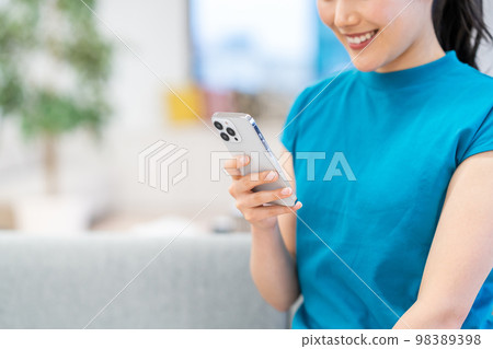 A young woman using a smartphone in the living room. (parts) A young woman using a smartphone in the living room. (parts) 98389398