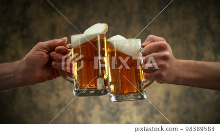 Two glasses of beer in cheers gesture, splashing. 98389583