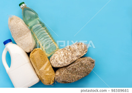 Food supply. Raw porridge, cereals, milk and vegetable oil on the blue table. Copy of space, flat. Food security for the poor Food supply. Raw porridge, cereals, milk and vegetable oil on the blue table. Copy of space, flat. Food security for the poor 98389681