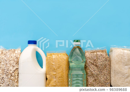 Food supply. Raw porridge, cereals, milk and vegetable oil on the blue table. Copy of space, flat. Food security for the poor 98389688