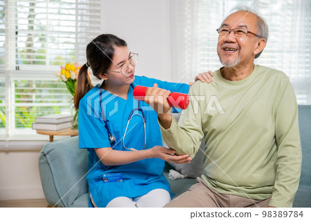 Asian nurse physiotherapist helping senior man in lifting dumbell at retirement home, Young nurse take care support training elderly sitting on sofa using dumbbell workout exercise, Healthcare medical 98389784