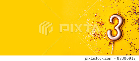 Gold candle in the form of number three on yellow background with confetti. Gold candle in the form of number three on yellow background with confetti. 98390912