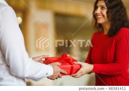 Man gives to his woman a gift box with red ribbon. A loving couple celebrating Valentine's Day. Man gives to his woman a gift box with red ribbon. A loving couple celebrating Valentine's Day. 98391411