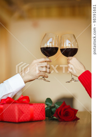 Couple clink glasses with red wine. Lovers give each other gifts. Romantic dinner. Relationship. Couple clink glasses with red wine. Lovers give each other gifts. Romantic dinner. Relationship. 98391681