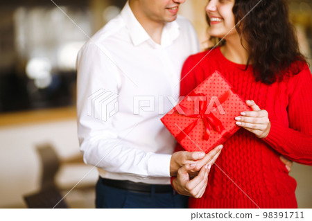 Man gives to his woman a gift box with red ribbon. A loving couple celebrating Valentine's Day. Man gives to his woman a gift box with red ribbon. A loving couple celebrating Valentine's Day. 98391711