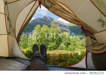 Guy is looking from the tent to the mountains 98392119