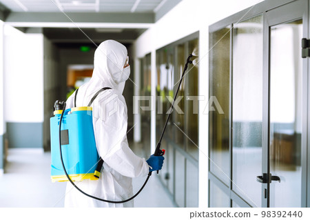Contractor disinfecting office for COVID-19 coronavirus. A disinfector in a protective suit and mask Contractor disinfecting office for COVID-19 coronavirus. A disinfector in a protective suit and mask 98392440