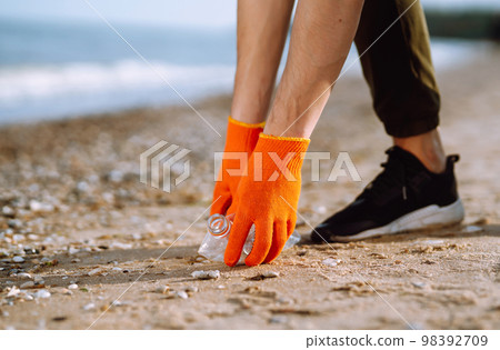 Trash on the beach. Men hand wearing protective gloves collects bottle plastic on sea beach. Trash on the beach. Men hand wearing protective gloves collects bottle plastic on sea beach. 98392709