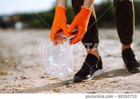 Trash on the beach. Men hand wearing protective gloves collects bottle plastic on sea beach. Trash on the beach. Men hand wearing protective gloves collects bottle plastic on sea beach. 98392710