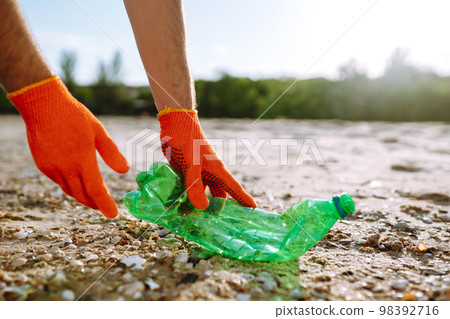 Trash on the beach. Men hand wearing protective gloves collects bottle plastic on sea beach. Trash on the beach. Men hand wearing protective gloves collects bottle plastic on sea beach. 98392716