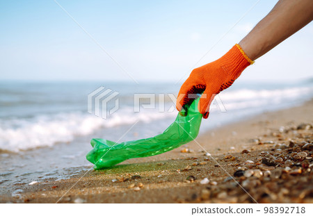 Trash on the beach. Men hand wearing protective gloves collects bottle plastic on sea beach. Trash on the beach. Men hand wearing protective gloves collects bottle plastic on sea beach. 98392718