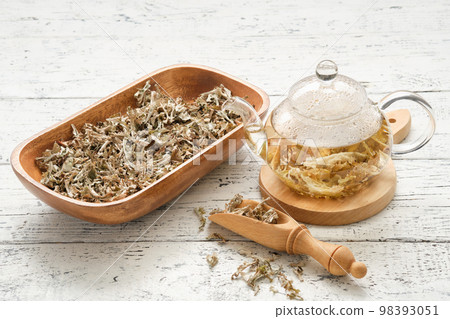 Glass teapot of herbal Icelandic moss tea. Wooden scoop and bowl of dried Iceland moss on white table. Cetraria islandica - latin name of plant. Alternative herbal medicine. Glass teapot of herbal Icelandic moss tea. Wooden scoop and bowl of dried Iceland moss on white table. Cetraria islandica - latin name of plant. Alternative herbal medicine. 98393051