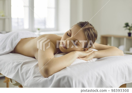 Beautiful relaxed young woman lying on massage table after back massage in spa salon. 98393308