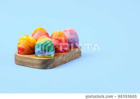 Colorful Easter eggs in a wooden egg stand on a blue background with a place for text. Happy Easter concept. Greeting card. Colorful Easter eggs in a wooden egg stand on a blue background with a place for text. Happy Easter concept. Greeting card. 98393600