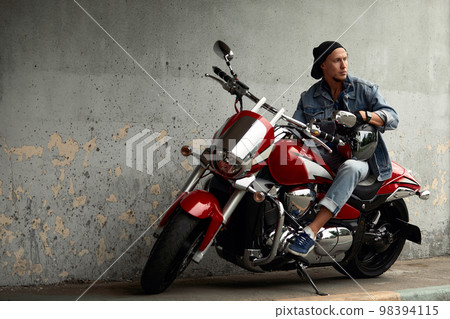 Handsome bearded biker with red motorcycle in classic style. Cafe racer in the garage. Handsome bearded biker with red motorcycle in classic style. Cafe racer in the garage. 98394115