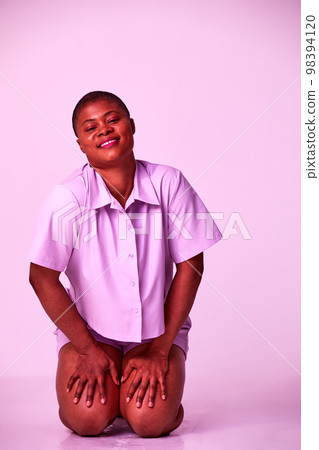 Overjoyed plus size millennial black woman in purple t-shirt and shorts sitting on floor relaxing isolated on purple studio background 98394120