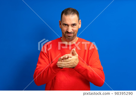 Latino handsome man feeling proud, mischievous and arrogant while hatching an evil plan or thinking up a trick. Isolated on blue background. Latino handsome man feeling proud, mischievous and arrogant while hatching an evil plan or thinking up a trick. Isolated on blue background. 98395290