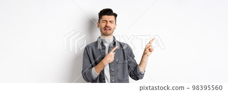 Sad crying man pointing fingers left at logo, sobbing and whining, being jealous or upset, standing on white background Sad crying man pointing fingers left at logo, sobbing and whining, being jealous or upset, standing on white background 98395560