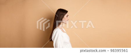 Profile of beautiful caucasian woman with long natural hair, looking left at empty space and smiling romantic, standing on beige background Profile of beautiful caucasian woman with long natural hair, looking left at empty space and smiling romantic, standing on beige background 98395561