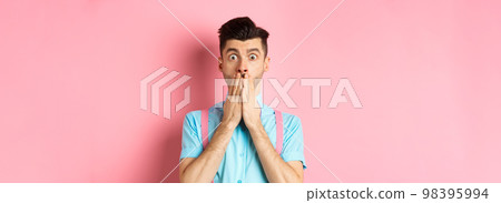 Shocked man looking in startled, covering mouth with hands and staring at camera, standing on pink background 98395994