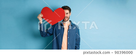 Happy man showing valentines heart and smiling, make romantic gift on lovers day, standing over blue background Happy man showing valentines heart and smiling, make romantic gift on lovers day, standing over blue background 98396000