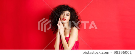 Romantic sensual woman with curly hair, wearing evening dress, posing seductive on red background Romantic sensual woman with curly hair, wearing evening dress, posing seductive on red background 98396001