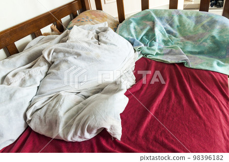 Unmade child bed with crumpled red and white bed linens and pillow. 98396182