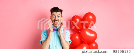 Love and romance concept. Happy man screaming from fantastic news, shouting wow and smiling amused, checking out special offer on Valentines, standing near red hearts balloons Love and romance concept. Happy man screaming from fantastic news, shouting wow and smiling amused, checking out special offer on Valentines, standing near red hearts balloons 98396183