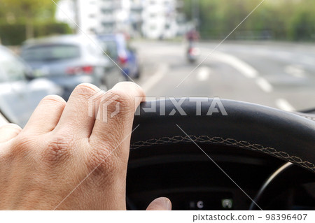 Steerind wheel with driver hand on it in modern car interior with view of street Steerind wheel with driver hand on it in modern car interior with view of street 98396407